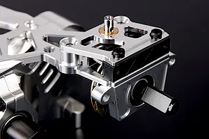 Close-up of a silver aluminium RC transmission assembly with black hex drive and metal components on a dark background.