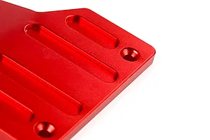 A close-up view of a red anodized aluminium front skid plate for an RC vehicle, showing machined slots and countersunk screw holes.