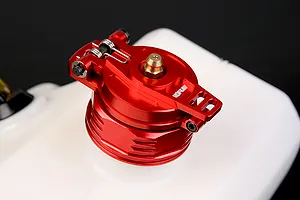 A red anodized aluminium fuel tank cap with a spring-loaded latch mechanism, mounted on a white plastic RC fuel tank.