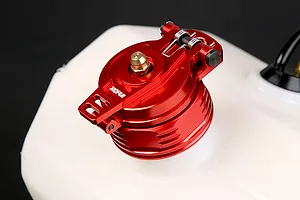A red anodized aluminium fuel tank cap with a spring-loaded latch mechanism, mounted on a white plastic RC fuel tank.