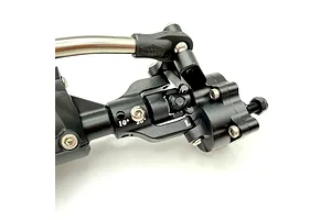 Close-up view of a black anodized aluminium RC portal axle assembly with steering linkage and universal joint on a white background.