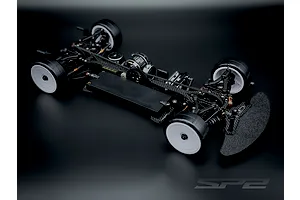 RC Maker SP2 EP 1/10 scale electric touring car chassis with carbon fibre deck and white wheels on dark background.