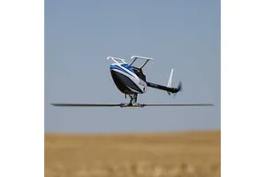 Blade InFusion 210 RC helicopter in flight against an open sky and field background.