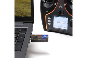 Spektrum wireless simulator USB dongle plugged into a laptop alongside an RC transmitter on a white surface.