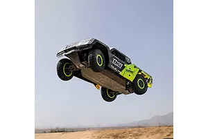 Losi 1/5 scale 5IVE-TG 3.0 petrol RC short course truck jumping high into the air above a dirt track against a clear sky.