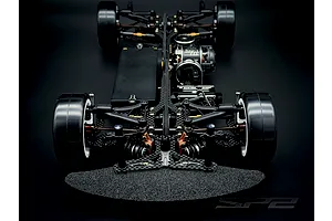 Top down front view of the RC Maker SP2 EP RC Touring Car chassis showing carbon fiber deck, suspension, and electronics on a dark background.