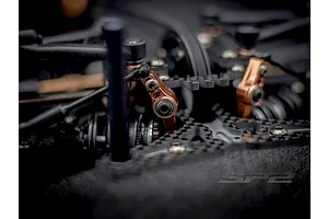 Close-up of RC Maker SP2 EP RC touring car chassis featuring carbon fiber parts and bronze metal linkage components.