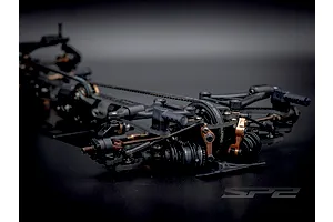 Close-up angled view of the front suspension and chassis components of the RC Maker SP2 1/10 scale electric touring car kit.