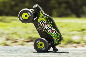 ARRMA Gorgon Grom RC monster truck performing a wheelie outdoors on a paved surface.