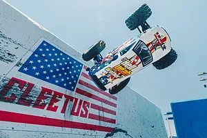 ARRMA Freedom Flyer 223S BLX RC monster truck performing an aerial jump past a painted US flag wall outdoors.