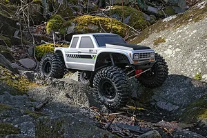 Axial SCX10 III Coyote silver RC rock crawler driving over rough mossy rocks outdoors