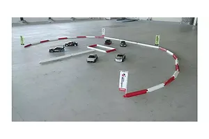 An RC circuit setup on a concrete floor using white and red fence barriers and miniature drift cars.