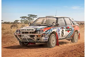 A Lancia Delta Integrale rally car driving on a dusty dirt road in an African savanna with zebras in the background.