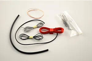 Model kit parts including various wires, tubing, coiled springs, and hardware in a plastic bag on a white background.