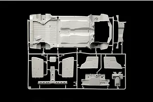 A light grey plastic model kit runner containing a car chassis floorpan and interior panel parts against a black background.