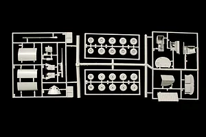 Grey plastic model kit sprues showing various parts and multiple wheels on a black background.