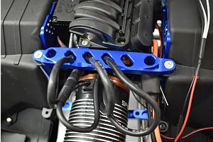 Close-up view of a blue anodized aluminium front chassis brace installed on an RC car, with wires running over it.
