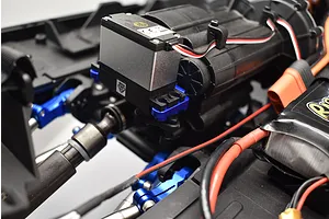 Close-up of an RC car chassis showing a blue aluminium 2-speed transmission servo mount installed near the transmission and servo.