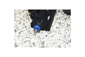 Blue anodised aluminium wheel hex adaptor installed on an RC car suspension arm over a concrete background.