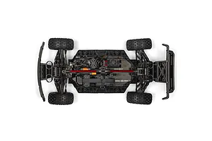 Top-down studio view of the RC short course truck chassis showing electronics layout, battery strap, and shock absorbers.