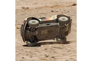 ARRMA Mojave 6S RC short course truck flipping and sliding on a dirt track, showing its scratched chassis plate.