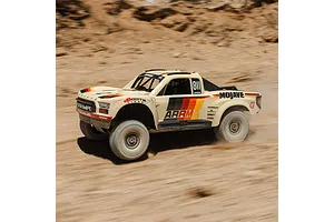 ARRMA Mojave 6S beige RC short course truck driving fast through a dusty desert landscape kicking up sand.
