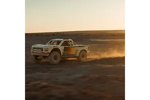 ARRMA Mojave 6S RC short course truck driving fast through a dusty desert landscape at sunset.