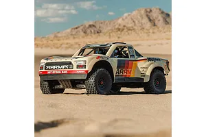ARRMA Mojave 6S beige RC short course truck driving on a sandy desert track with mountains in the background.