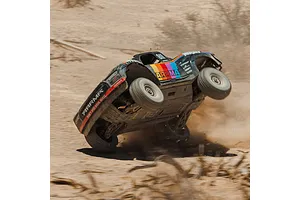 Action shot of an ARRMA Mojave 6S RC short course truck performing a wheelie on a dusty dirt track.