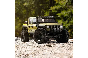 Green Axial SCX10 III RC rock crawler truck driving on a rocky outdoor trail with trees in the background.