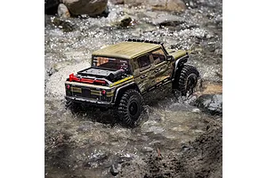 Axial SCX10 III RC rock crawler driving through shallow flowing water over rocky terrain outdoors.