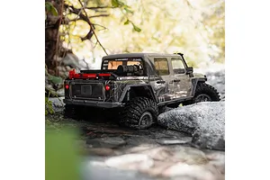 Axial SCX10 III Motobilt Valyrian Jeep JT Gladiator RC rock crawler driving through a shallow stream surrounded by rocks and foliage.