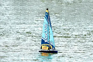 Joysway Focus V3 blue RC sailboat racing yacht gliding across open water with sunlight glinting on the surface.