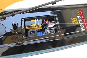 Close-up of the open electronic hatch on the deck of a black Joysway Focus V3 RC sailboat showing internal electronics and battery pack.