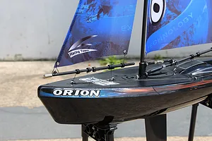 Close-up of the bow and rigging of the Joysway Orion V2 RC sailboat, showing its black hull and blue printed sails.