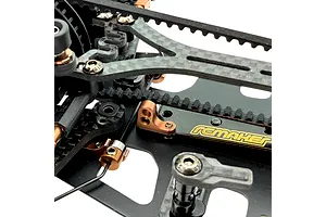 Close-up view of an RC Maker rear belt tensioner and carbon fiber chassis components on an RC car.