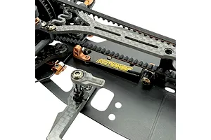 Close-up studio view of an RC Maker rear belt tensioner installed on an RC car chassis with carbon fiber parts.