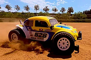 Yellow and blue Volkswagen RC buggy kicking up dust on a dirt track outdoors.