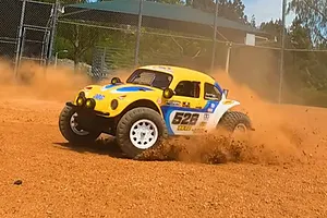 Tamiya BB-02 Volkswagen Dune Beetle RC buggy driving on a dirt track, kicking up dust and dirt.