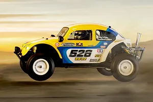 Side profile of a yellow and white Tamiya BB-02 Volkswagen Dune Beetle RC buggy mid-air in an outdoor desert setting.
