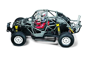 High angle side profile of the Tamiya BB-02 Volkswagen Dune Beetle RC buggy showing its roll cage, driver figures, and white wheels against a white background.