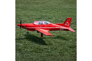 A red RC Pilatus PC-21 airplane taxies across a green grass field during an outdoor flight session.