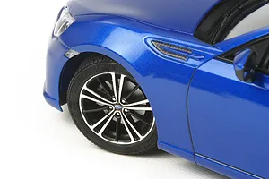 Close-up of the front left quarter of a blue Tamiya 1/24 scale Subaru BRZ model car, showing the wheel, fender, and side vent.