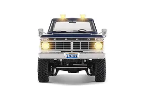 Front view of the FMS FCX18 II Ford F-100 RC rock crawler in blue and white with illuminated headlights, roof lights, and a Nevada license plate.