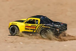 ARRMA Mojave Grom 4X4 RC Short Course Truck driving outdoors on a dirt track, kicking up dust and sand.