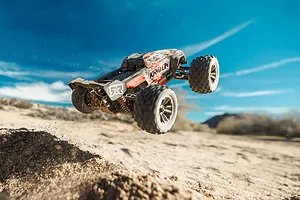 ARRMA Mini Kraton 3S BLX 4X4 RC monster truck airborne over a dirt jump in an outdoor setting against a blue sky.
