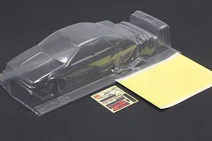 Clear unpainted polycarbonate RC car body shell with a sticker sheet and masking sheet on a dark background.