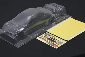 Clear unpainted polycarbonate RC car body shell with separate parts, decal sheet, and masking sheet on dark background.