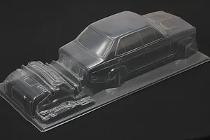 Clear unpainted polycarbonate RC car body shell for a 1/10 scale sedan with separate molded parts on a dark background.