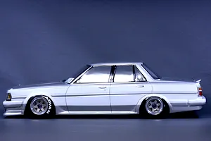 Side profile of a painted white and silver Toyota Cresta GX71 RC drift car body mounted on a chassis with custom wheels against a dark background.